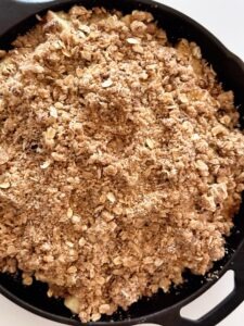 Close-up image of the dark brown sugar oat crumble topping packed into a cast iron skillet for apple crisp.
