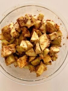 Bowl of Granny Smith apples mixed with cinnamon, dark brown sugar, vanilla, flour, and lemon juice for apple crisp.