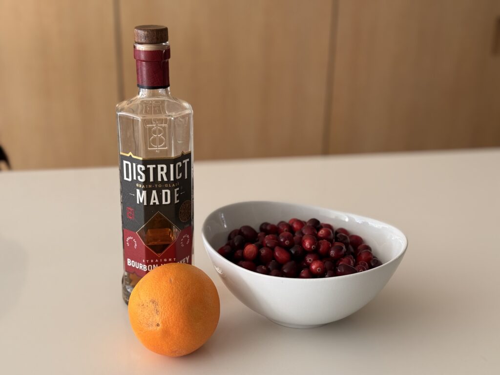 Ingredients for bourbon cranberry sauce including bourbon, fresh cranberries, and an orange
