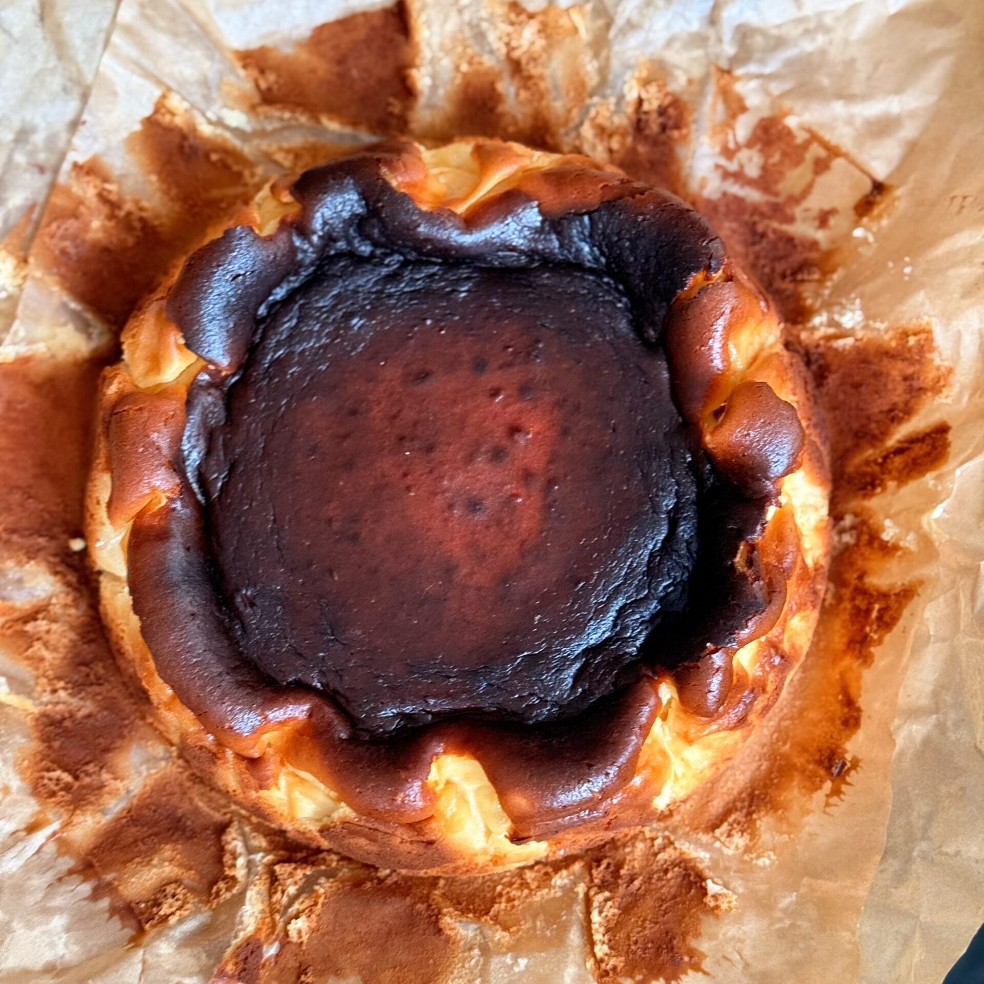 Burnt honey Basque cheesecake with a caramelized top, sliced on parchment paper beside a small bowl of honey.