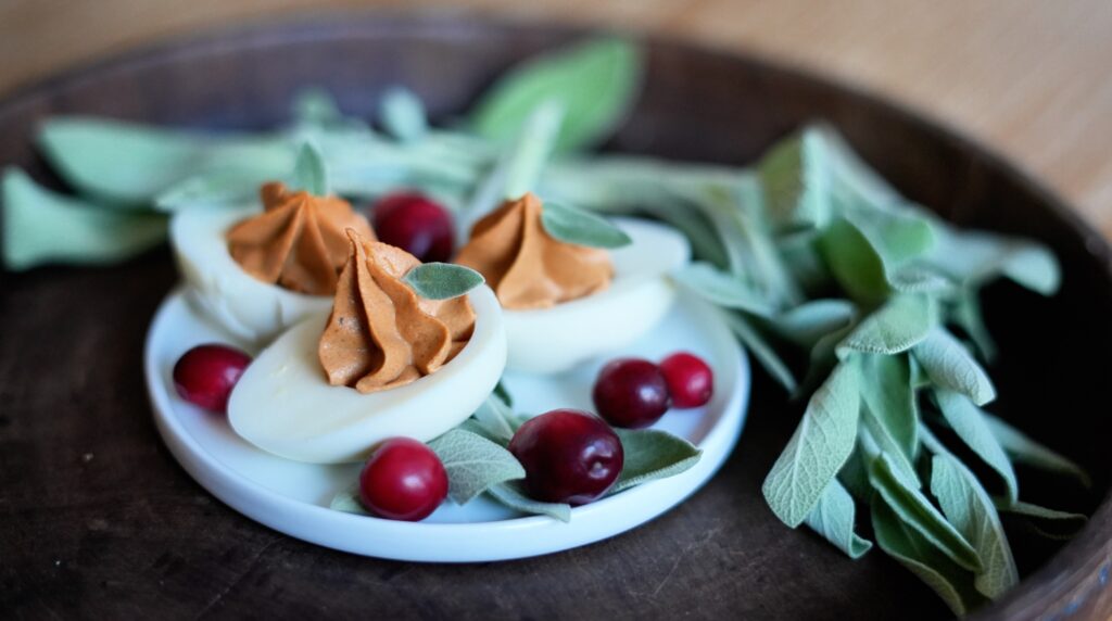 Close-up angled view of deviled eggs with cranberry filling and fresh sage garnish