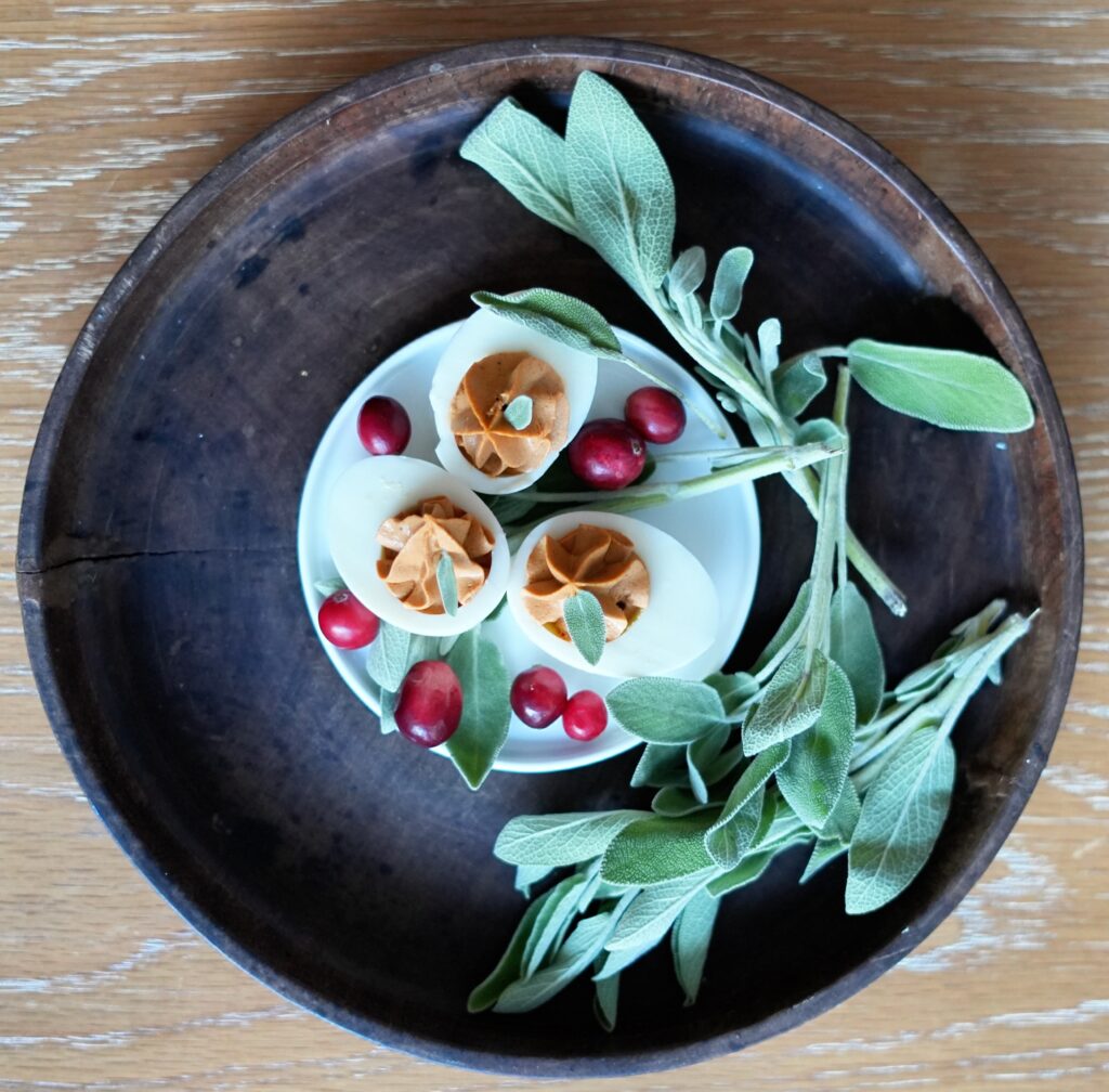 Side-angle view of cranberry-sage deviled eggs arranged with sage sprigs and cranberries