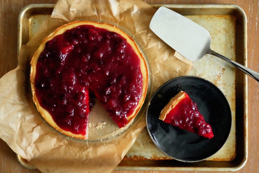 Overhead view of guava cranberry cheesecake with bright red fruit topping and lime on a sheet pan.