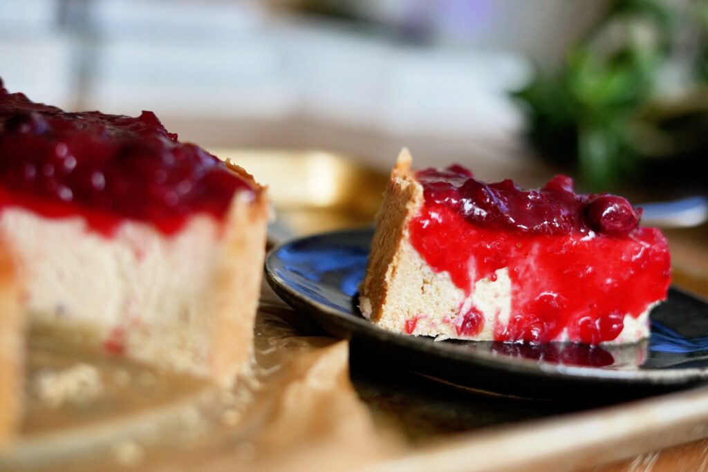 Side slice of guava cranberry cheesecake on a black plate showing creamy interior.