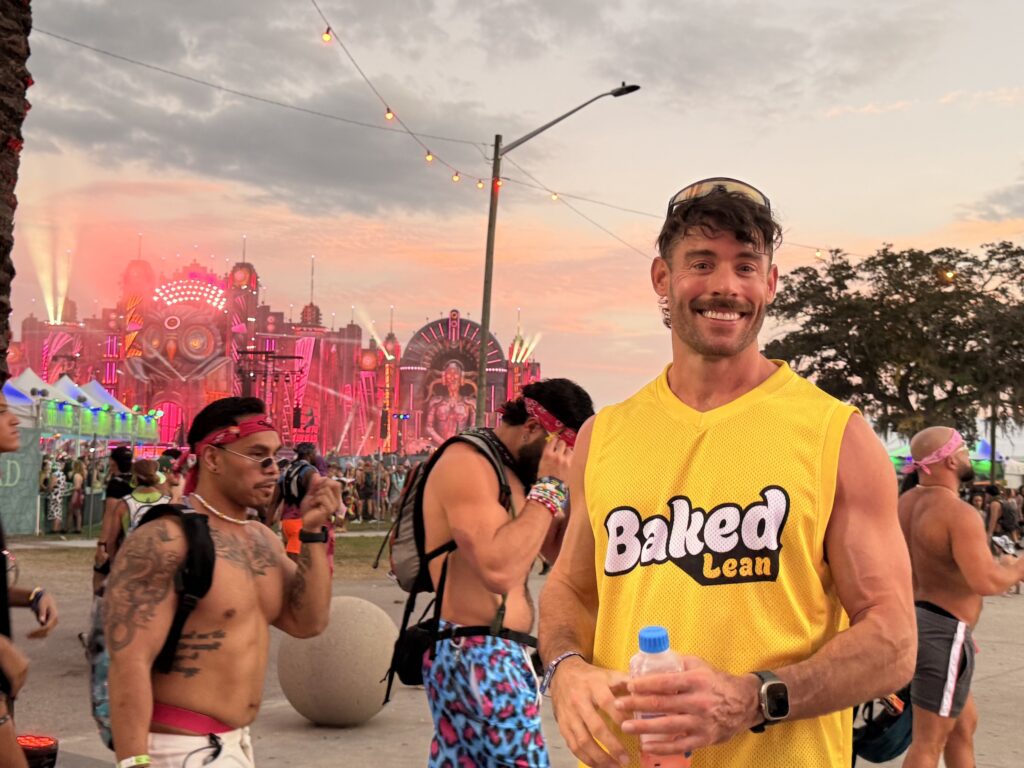 Jacob smiling in a yellow BakedLean jersey with the EDC Orlando festival stage in the background