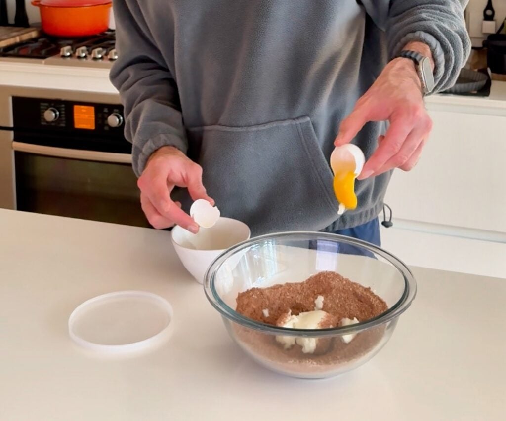 Adding egg yolk to chocolate almond flour tart crust mixture in a bowl.
