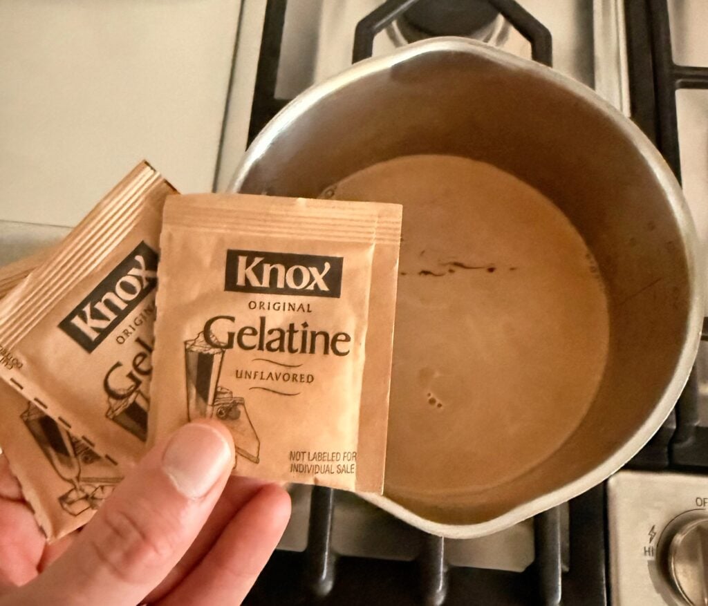 gelatin packets held over a saucepan of warm mocha protein shake