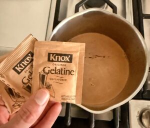 gelatin packets held over a saucepan of warm mocha protein shake