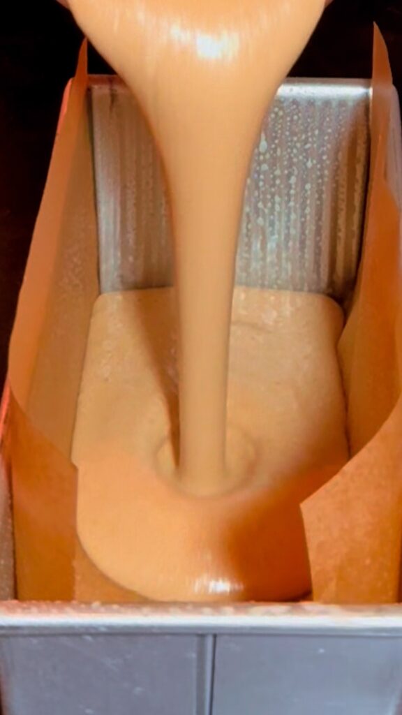 Smooth protein loaf batter being poured into a lined loaf pan.