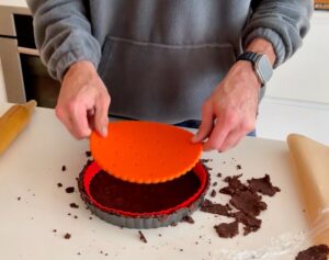 Pressing chocolate almond flour tart crust with silicone insert before baking.