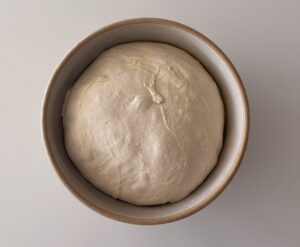 Smooth risen focaccia dough resting in a bowl after its first proof.