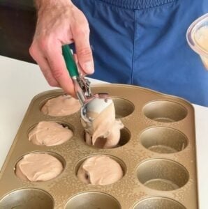 Muffin batter being scooped into a muffin tin using a cookie scoop