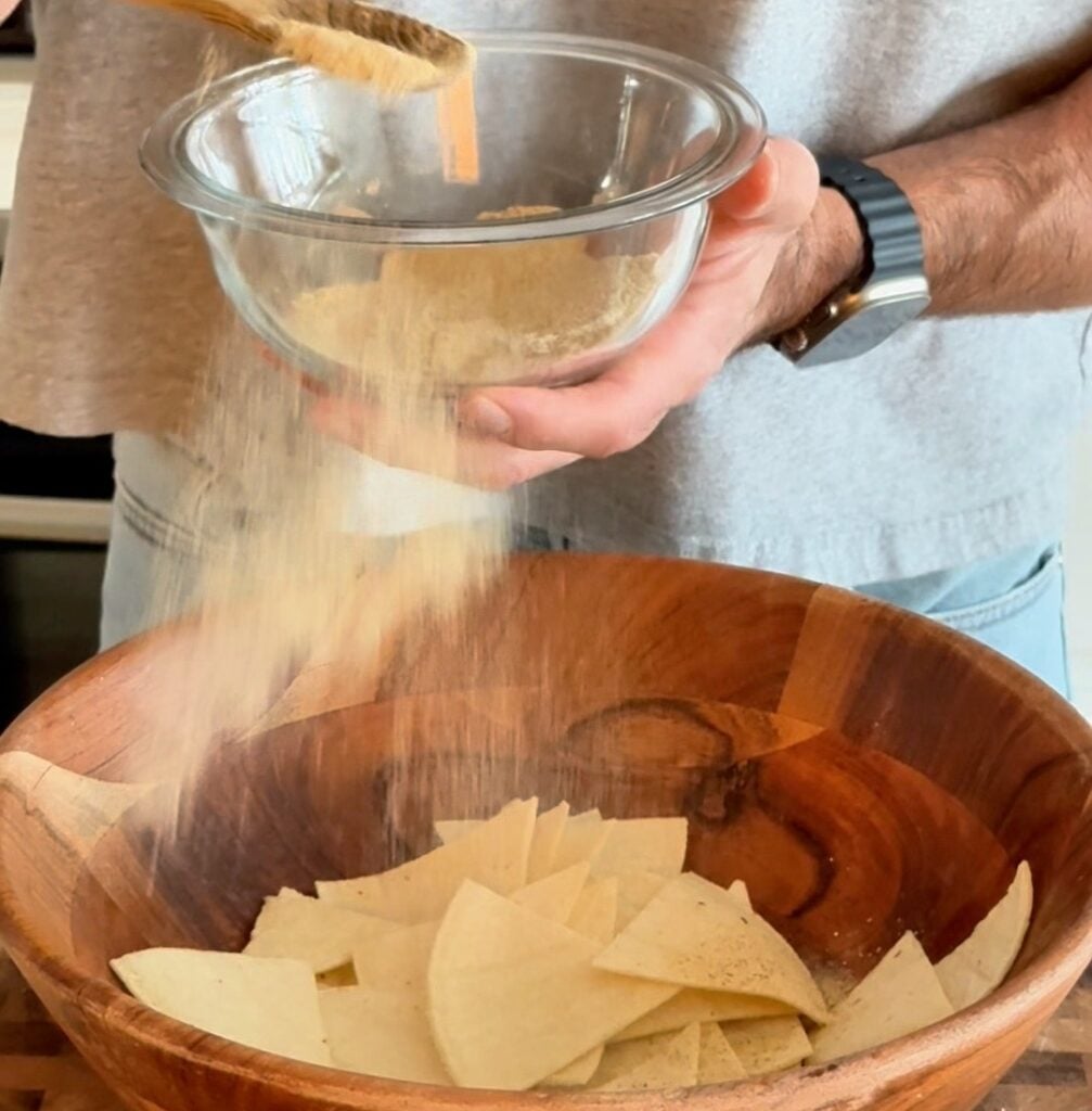 Pouring ranch seasoning mix into a bowl of tortilla chips before air frying