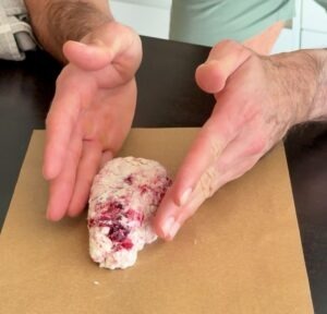 Hands shaping cranberry cottage cheese scone dough on parchment paper