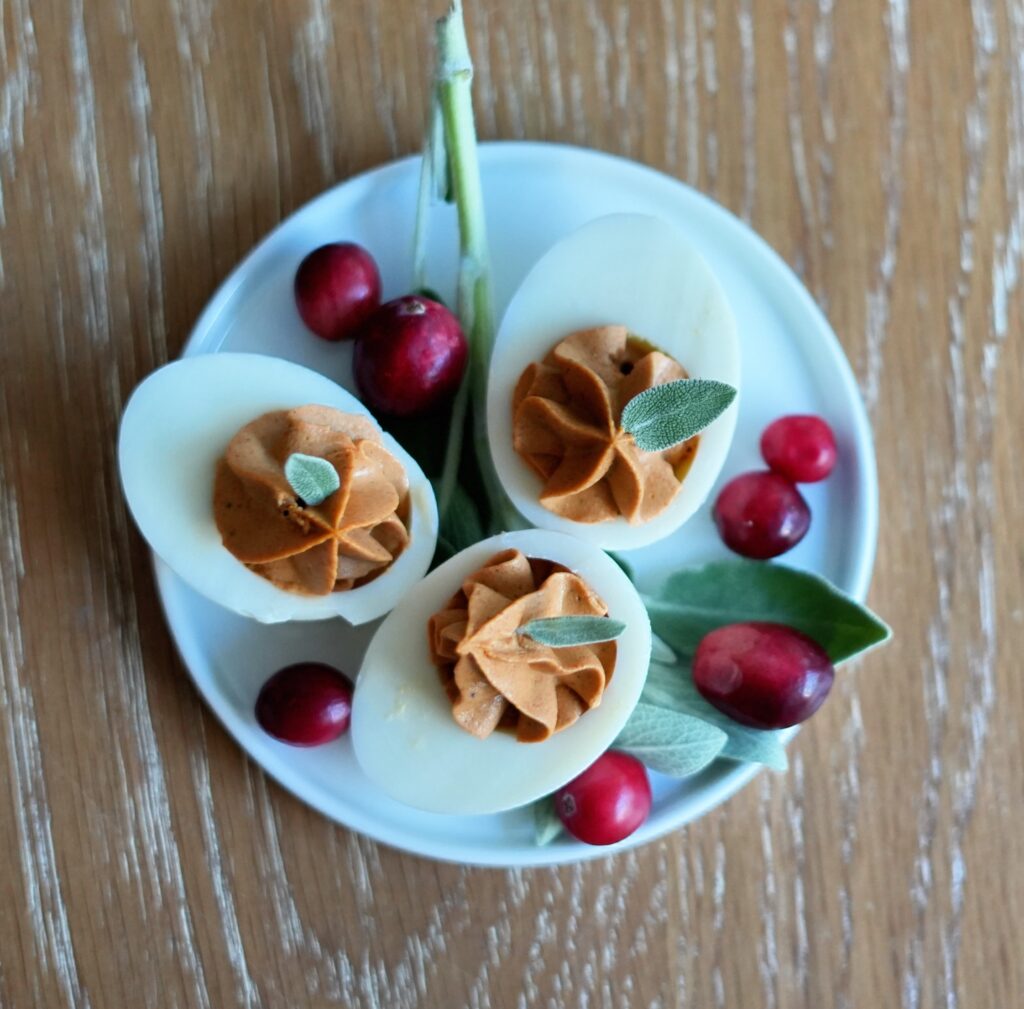 Overhead photo of cranberry-sage deviled eggs on a white plate surrounded by fresh sage