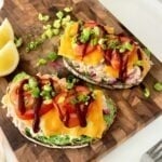 Open-face tuna melt on spinach bread topped with cheddar, tomato slices, sauce, and green onions