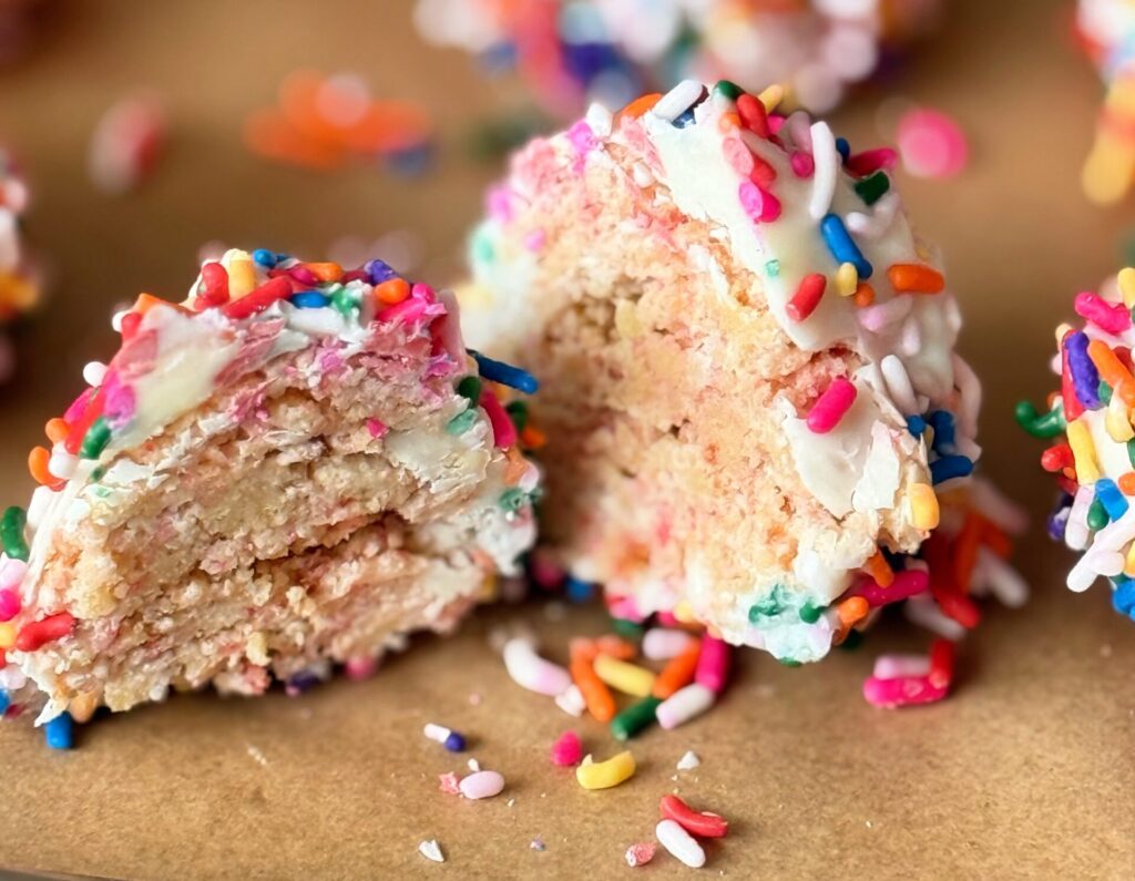 Several sprinkle-covered cake pops lined up on a baking tray