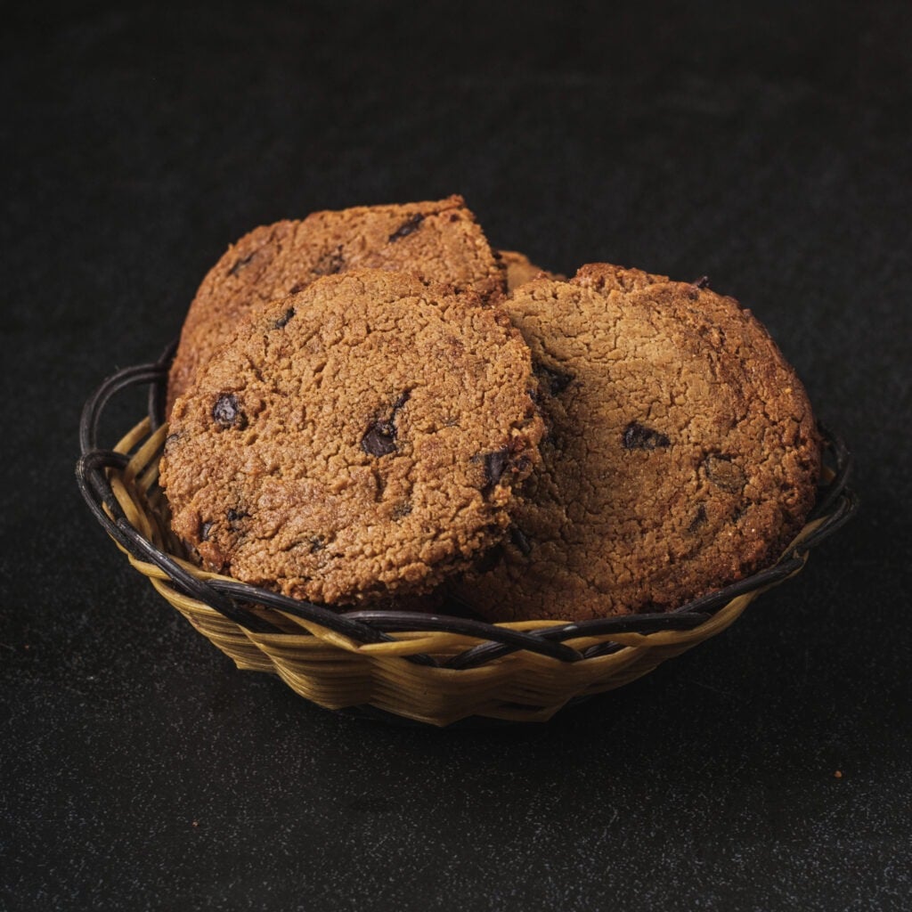 Vegan chocolate chip cookies stacked in a bowl on a dark background