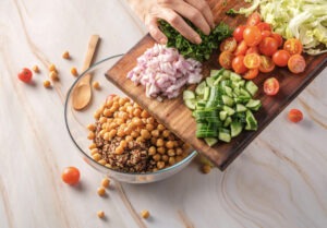 Cooked quinoa and chickpeas being poured into a glass mixing bowl, forming the protein-rich foundation of the salad.