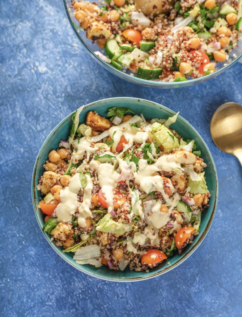Overhead shot of a large bowl of fresh vegan salad, featuring mixed greens, quinoa, chickpeas, and a drizzle of creamy, dairy-free tahini dressing.