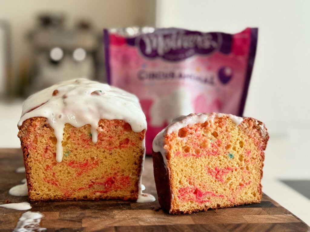 A close-up cross-section of a moist, fluffy, high-protein iced animal cracker loaf cake showing the pink/white crushed cookies embedded in the crumb.