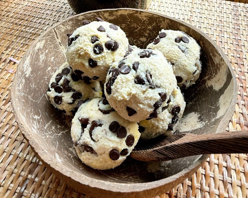 High-protein no-bake cookie dough served in a coconut bowl with chocolate chunks on top.