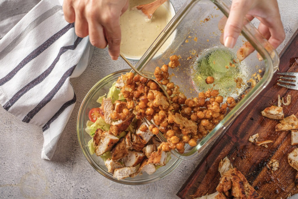Hands preparing the high-protein Greek yogurt Caesar dressing with a bowl of crispy Parmesan chickpeas.