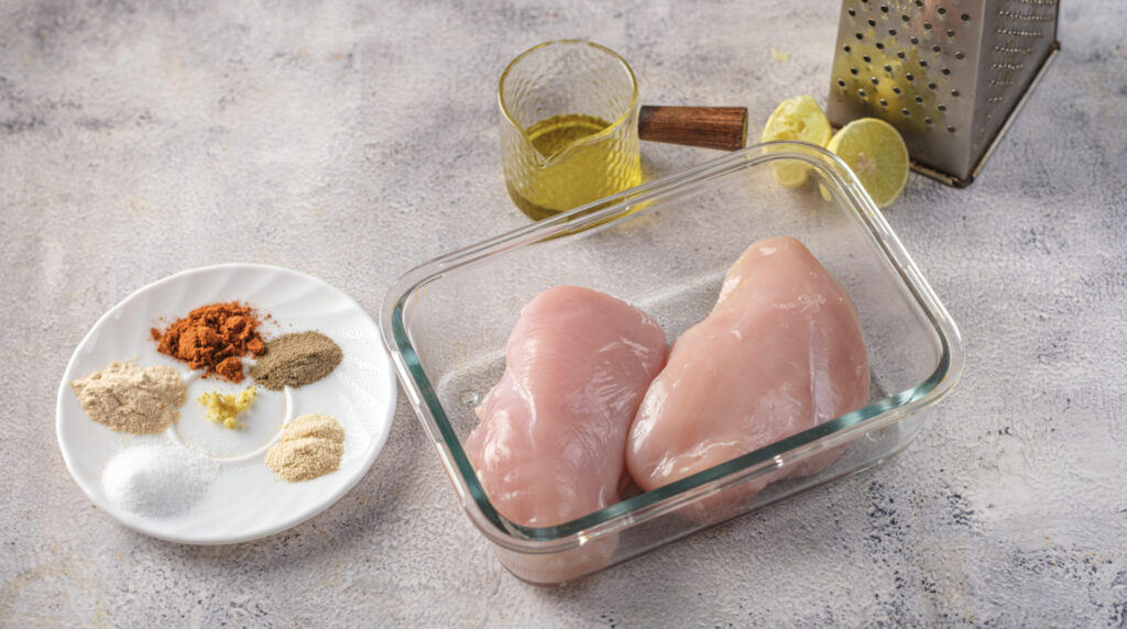 Two raw boneless chicken breasts placed in a glass dish, ready for the smoky marinade.