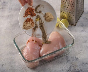 Grating lemon zest over the two chicken breasts in a glass dish for the smoky grilled chicken marinade.