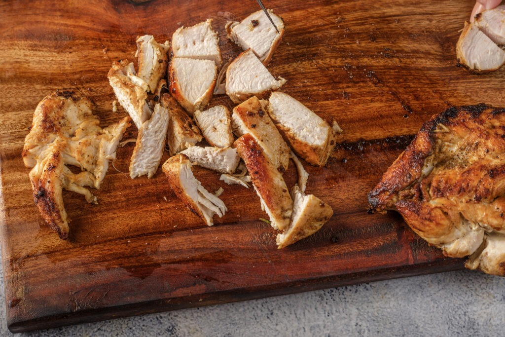 Sliced grilled chicken breast on a wooden cutting board, showing the smoky char and juicy interior.