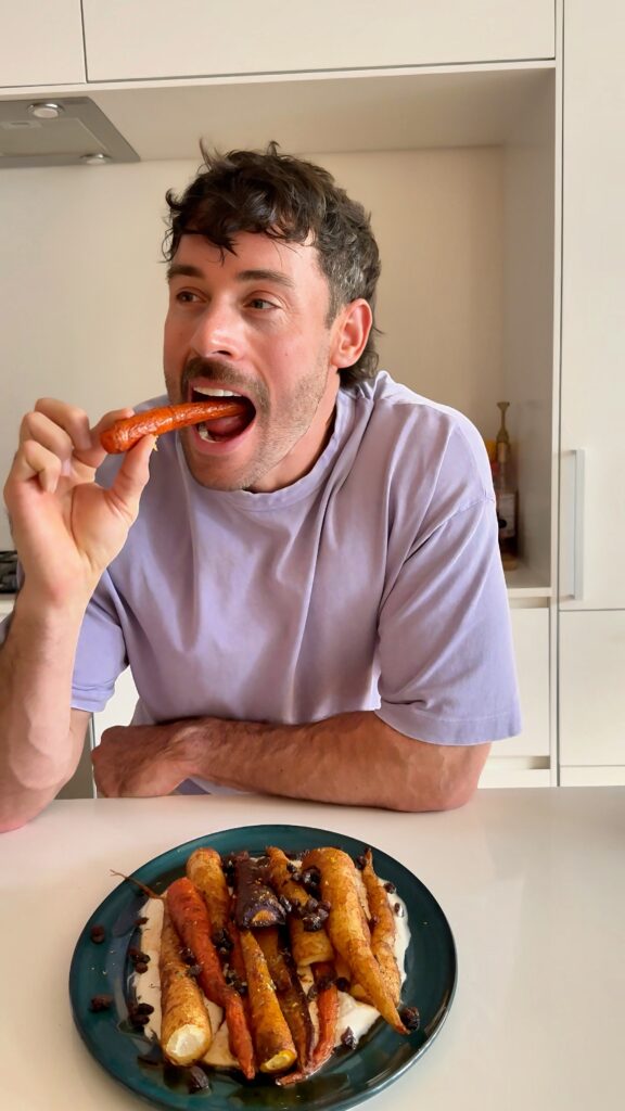Jacob eating a harissa and maple glazed carrot over spicy yogurt sauce