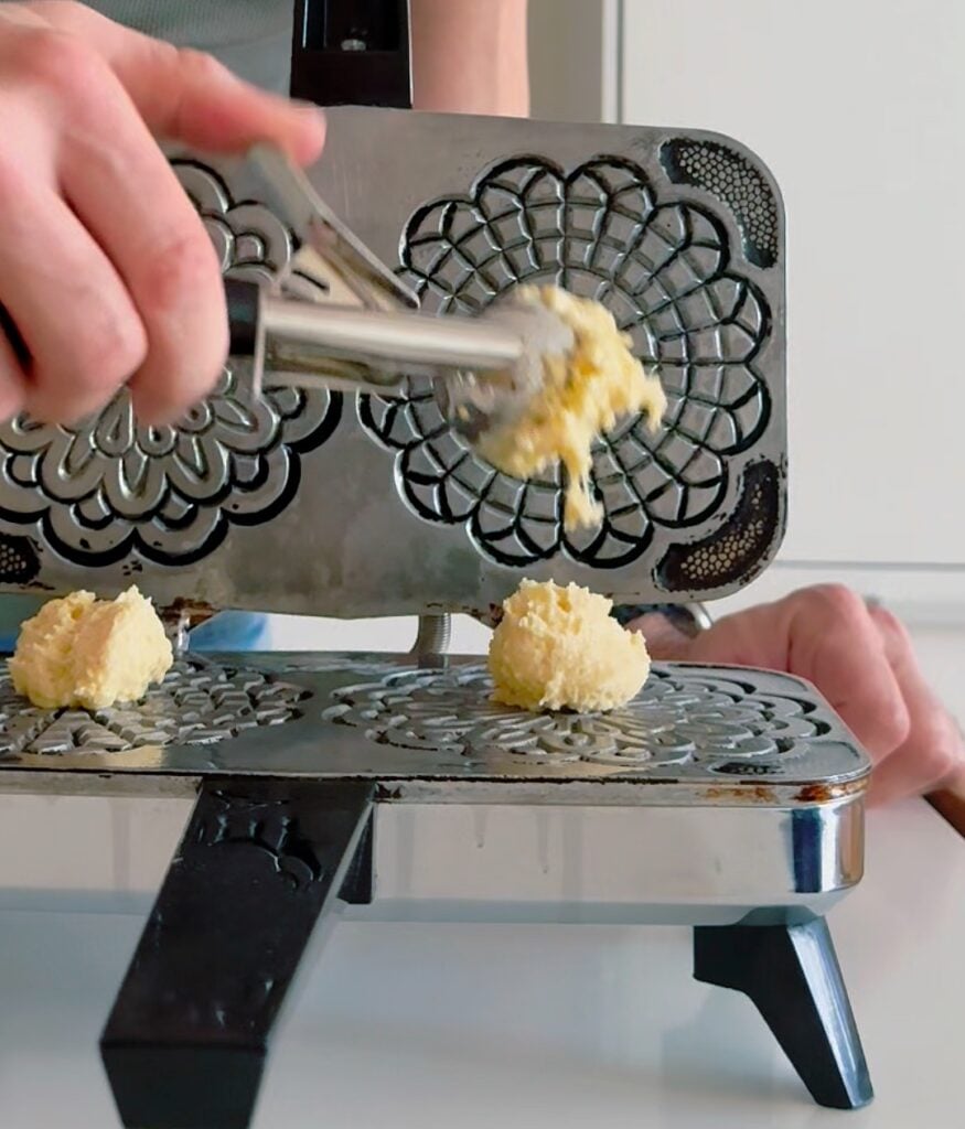 High-protein pizzelle batter pressed and cooking in a traditional pizzelle iron.