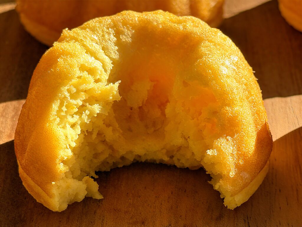 Close-up of a mini Bundt cake with a bite taken out, showing the moist, dense, golden interior crumb.