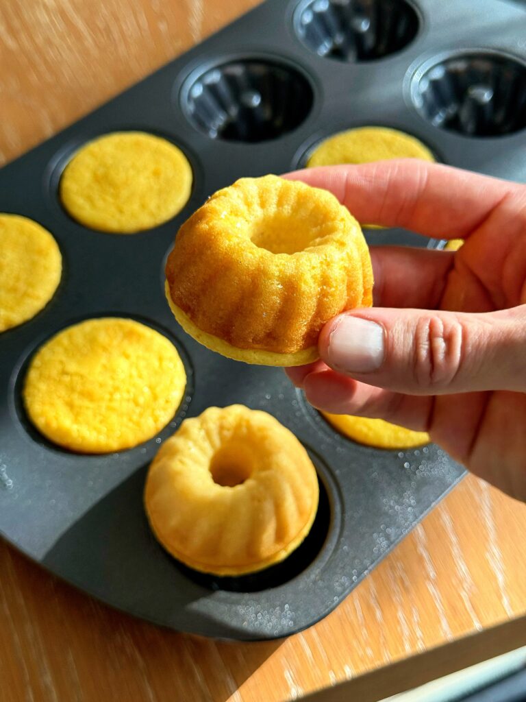 Hand removing a perfectly baked, golden mini Bundt cake from the non-stick mold pan.
