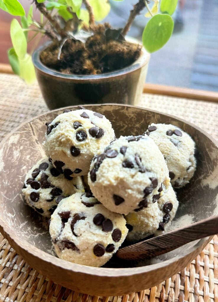 Close-up of creamy no-bake protein cookie dough in a coconut bowl with chocolate chunks folded throughout.