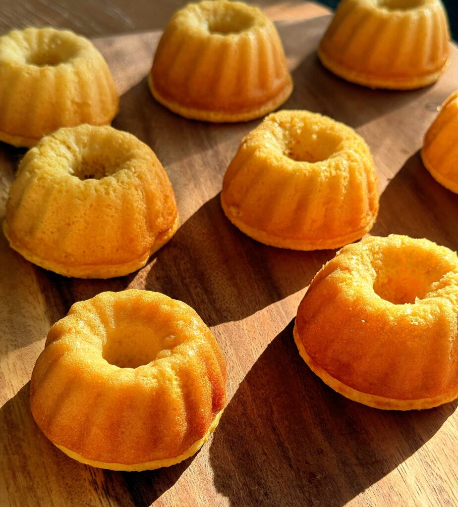 Batch of golden-orange mini Bundt cakes on a wooden surface, ready for cooling and decorating.