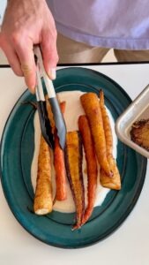 Plating roasted carrots with tongs for the harissa maple carrot recipe