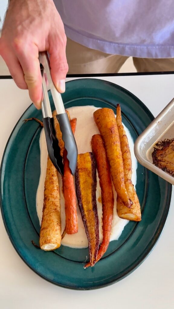 Plating roasted carrots with tongs for the harissa maple carrot recipe