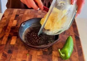 Pouring cornbread protein batter into a small cast iron skillet with jalapeños