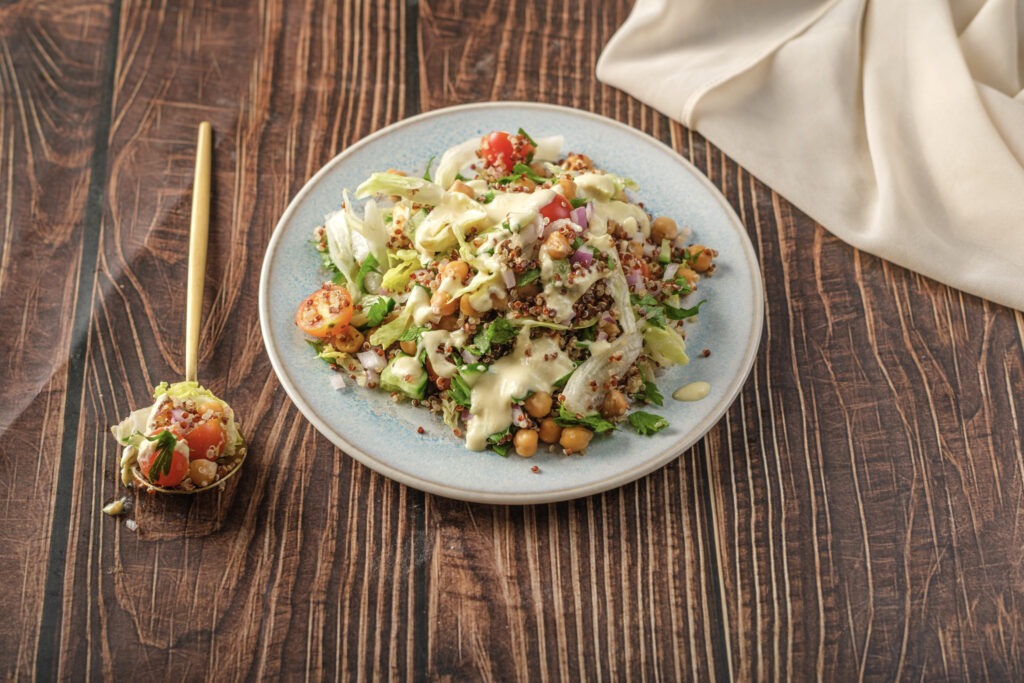 A vibrant, high-protein vegan quinoa salad topped with creamy lemon-tahini dressing, crispy baked tofu croutons, and chopped parsley.