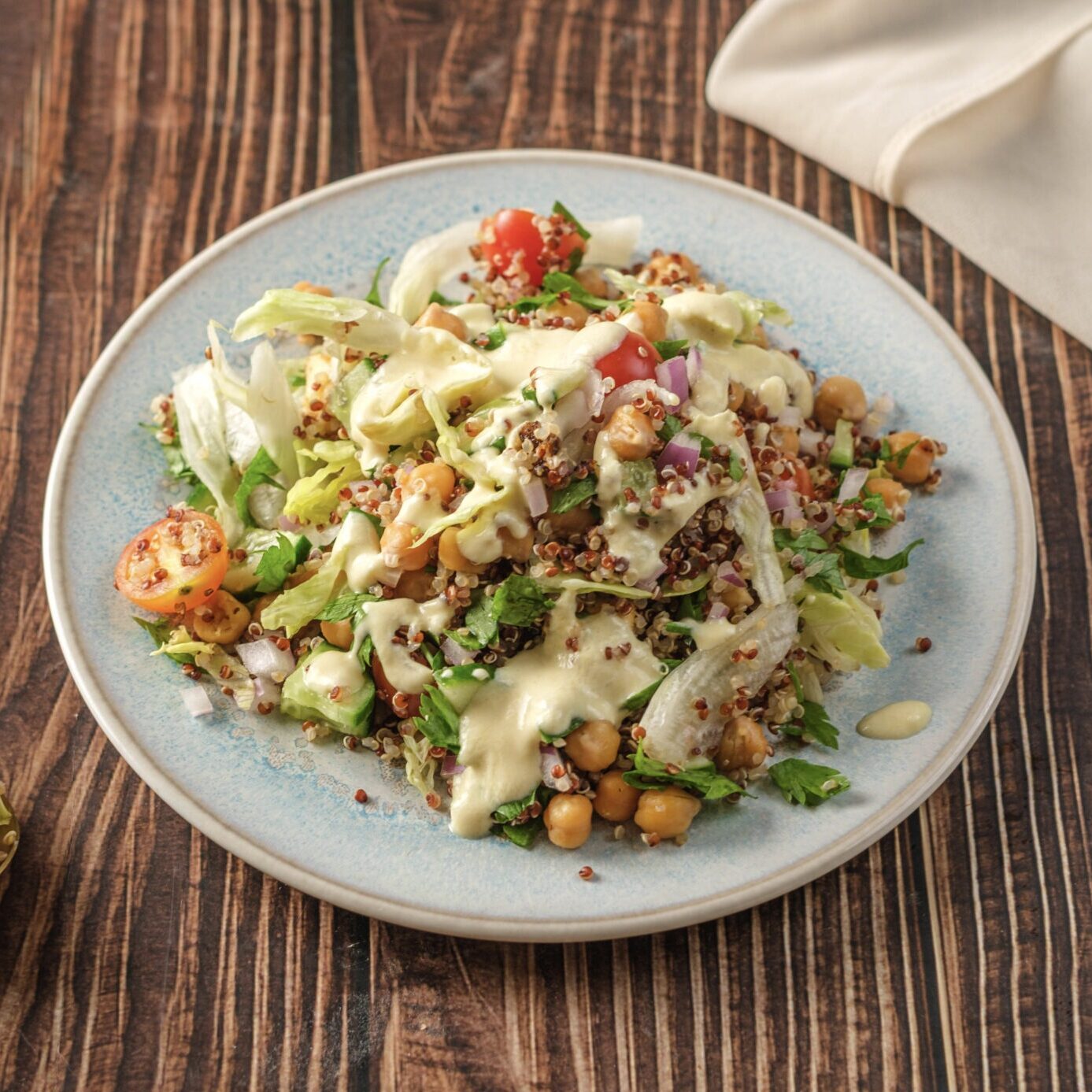 A vibrant, high-protein vegan quinoa salad topped with creamy lemon-tahini dressing, crispy baked tofu croutons, and chopped parsley.