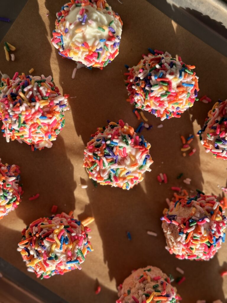 Colorful sprinkle-covered cake pops on parchment paper
