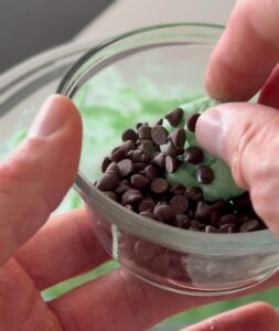 Hands rolling a scoop of the green mint cookie dough mixture into perfectly portioned, small protein balls.