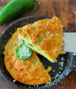 Cornbread in skillet sliced with spatula, showing moist, fluffy interior.
