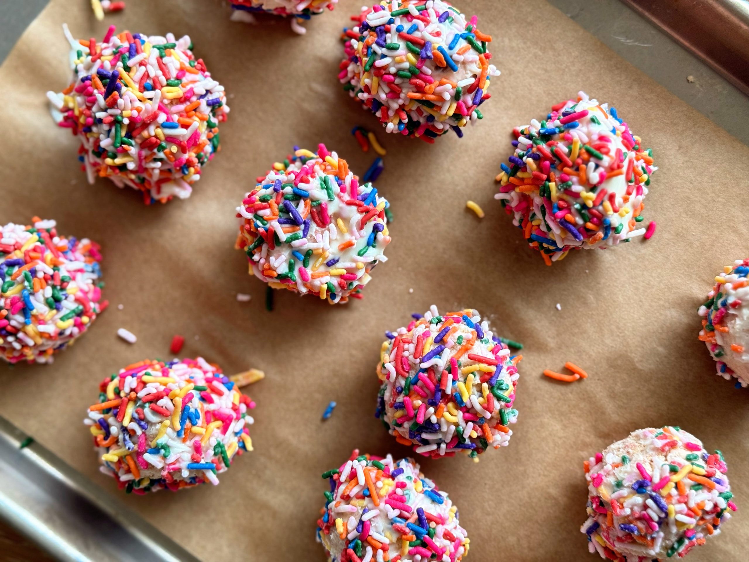 Several sprinkle-covered cake pops lined up on a baking tray