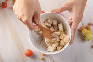 Hand tossing pressed tofu cubes with cornstarch, smoked paprika, and garlic powder to create a crispy coating.