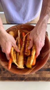 Tossing raw rainbow carrots in a bowl with seasoning