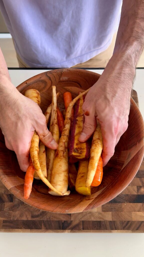 Tossing raw rainbow carrots in a bowl with seasoning