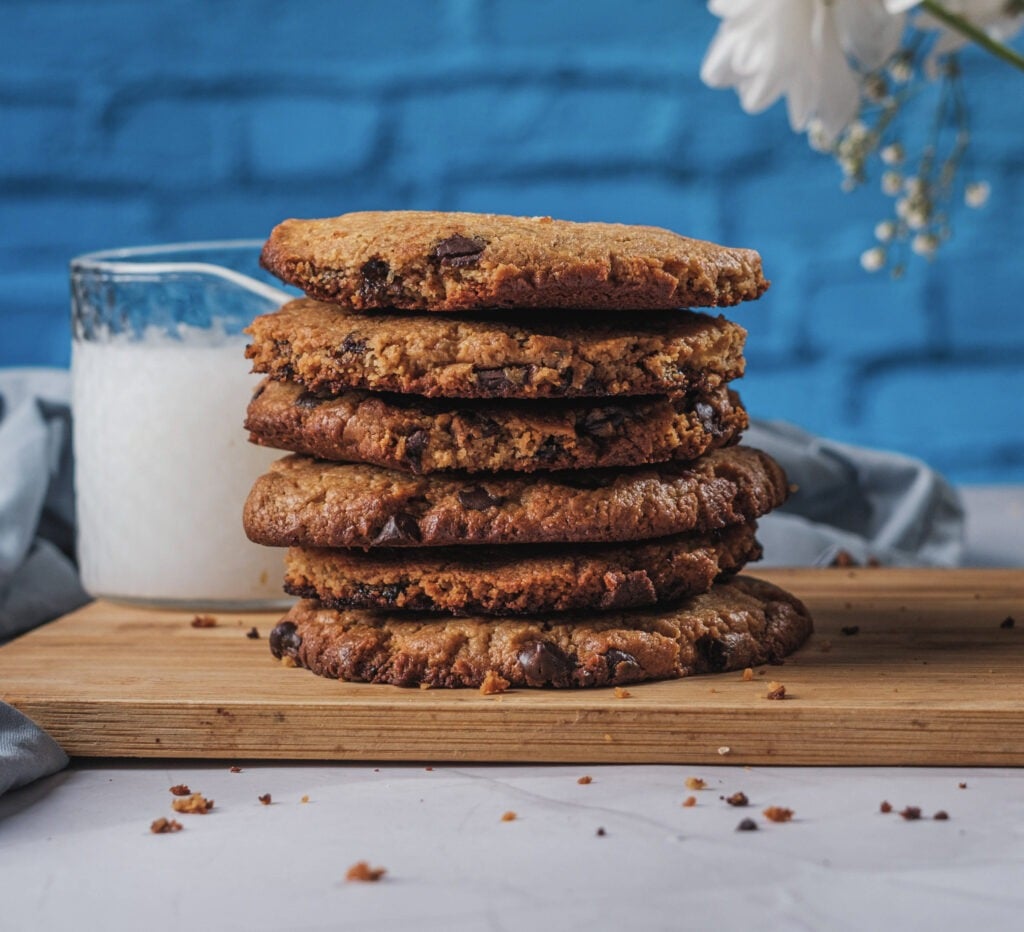 Vegan chocolate chip cookies stacked on a wooden board with a glass of milk