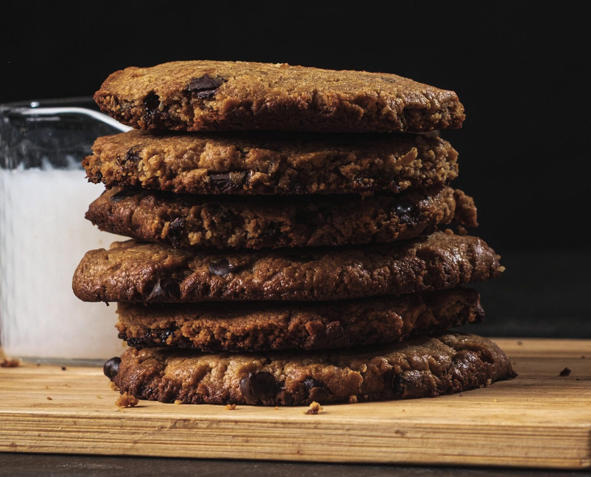Vegan chocolate chip cookies stacked on a wooden board with a glass of milk